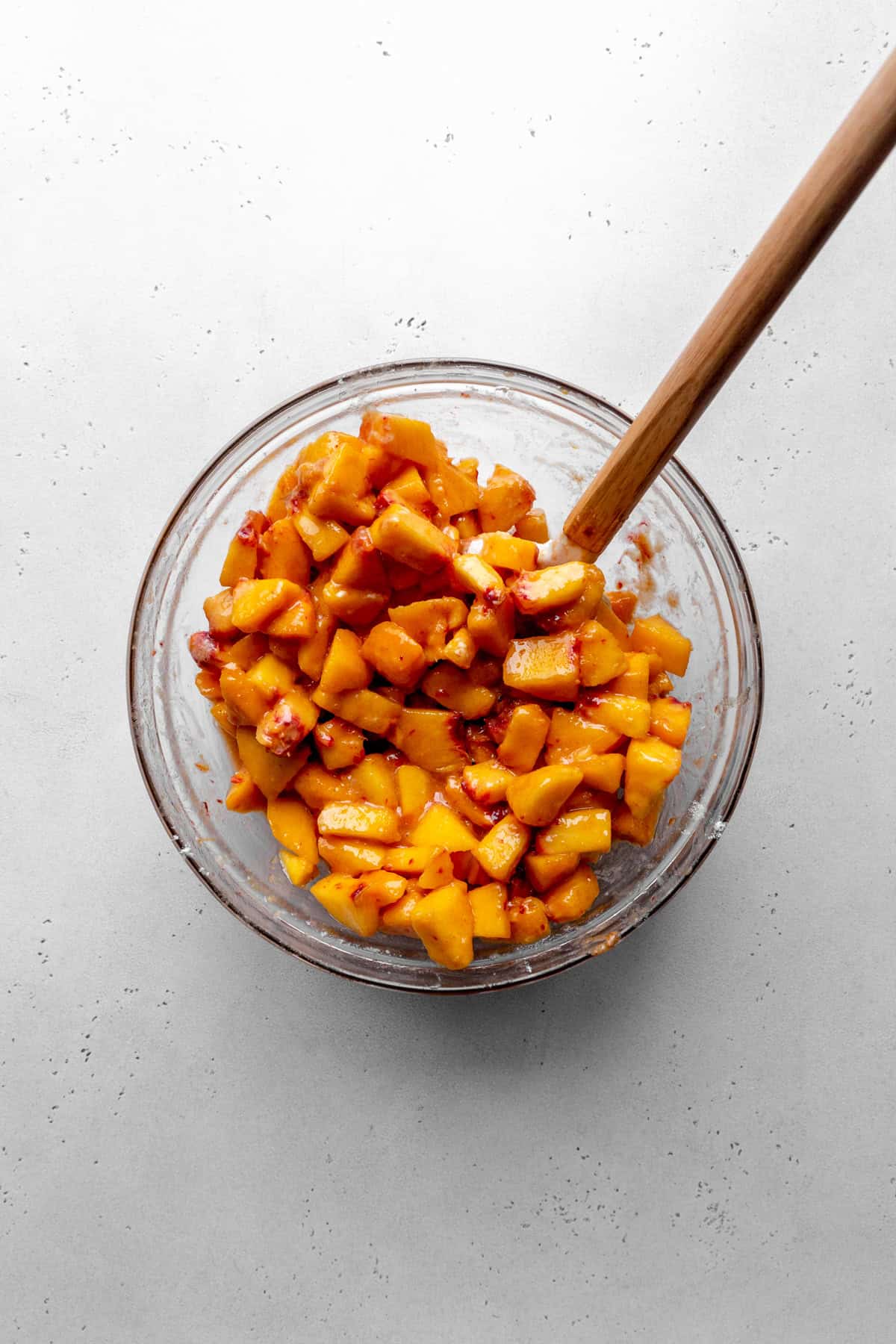 Glass bowl of cut and peeled peaches and a rubber spatula.