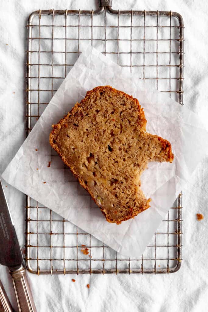 Slice of banana bread with a bite taken out of it on a wire rack.