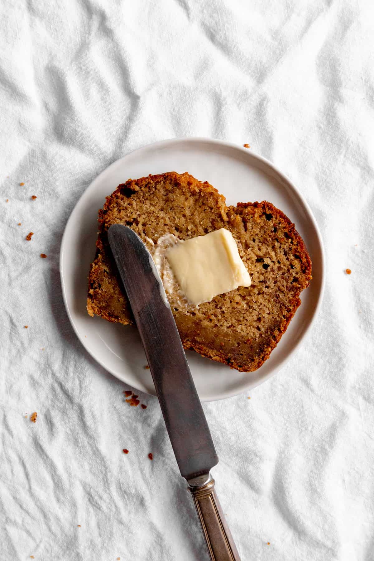 Knife spreading butter on a slice f banana bread.
