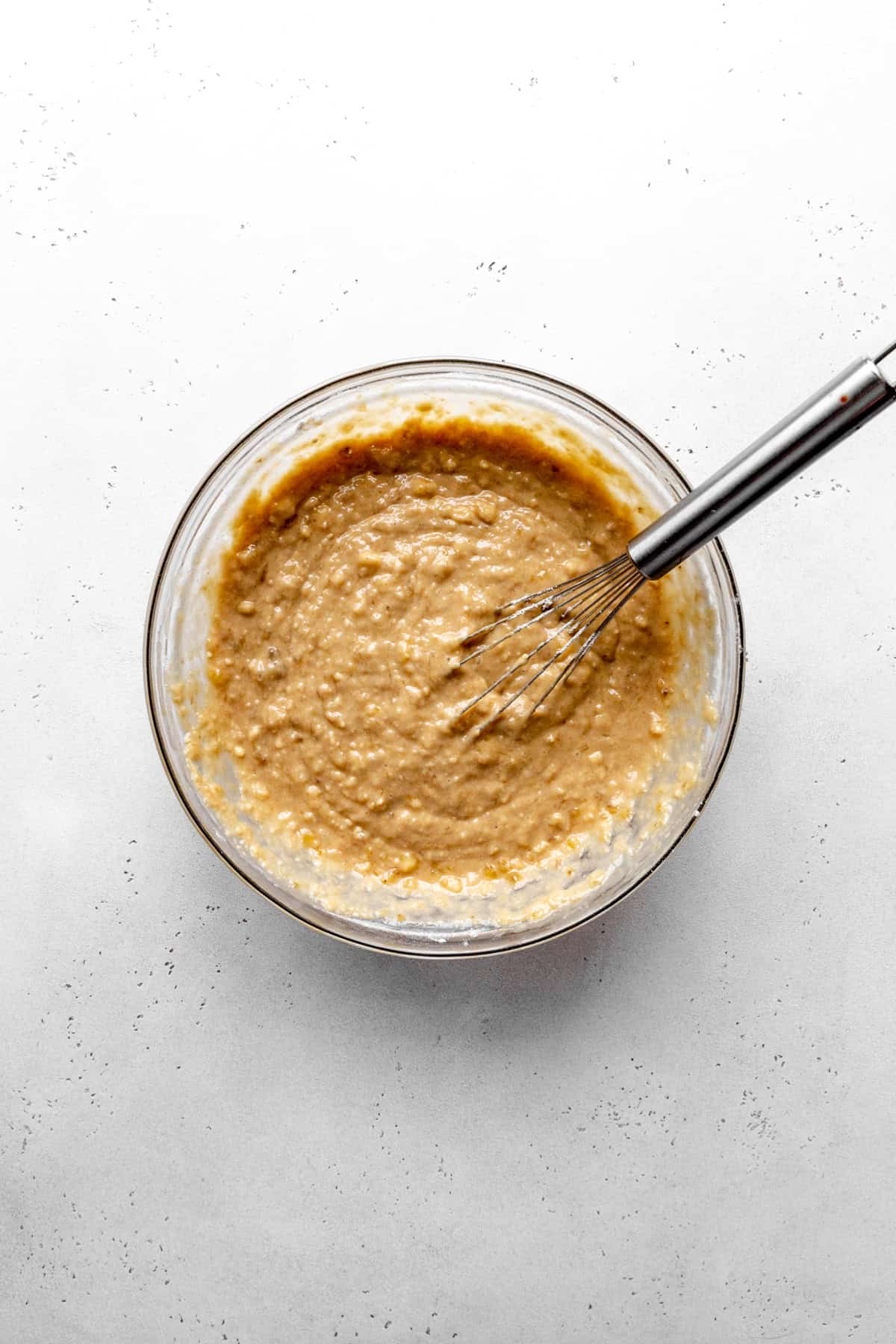 Glass bowl of banana bread batter and a whisk.