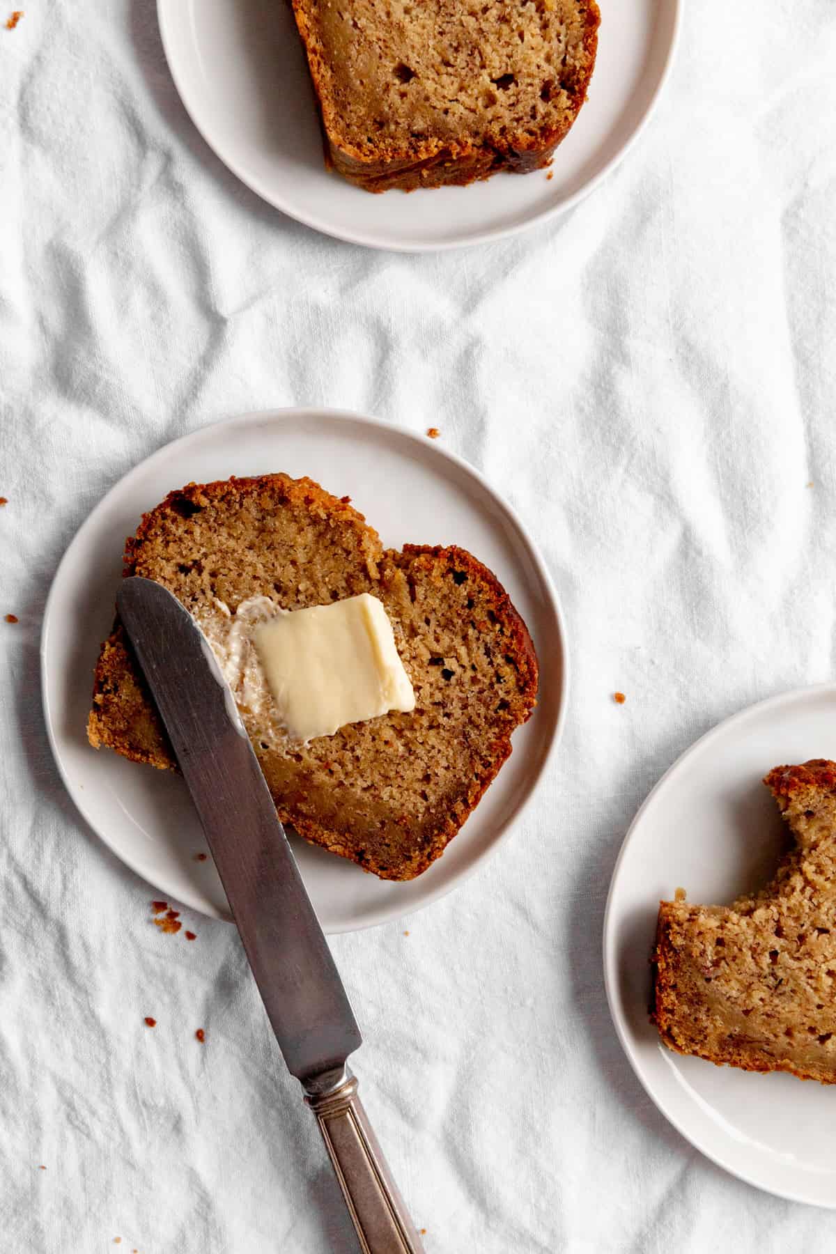 Knife spreading butter on a slice f banana bread.