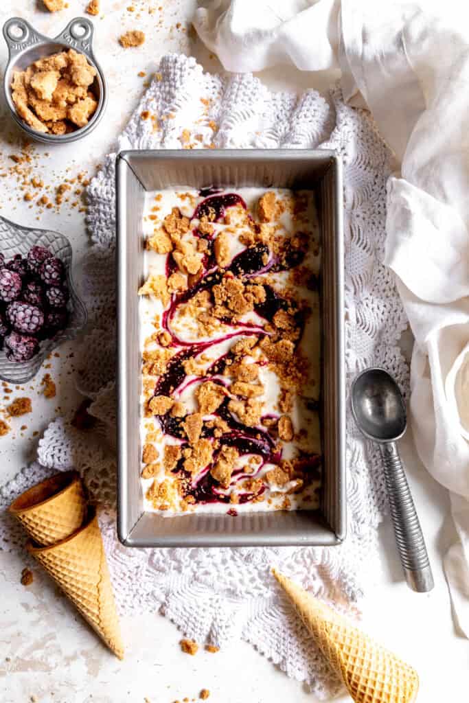 Blackberry cobbler ice cream in a loaf pan, a cup of blackberries and sugar cones.