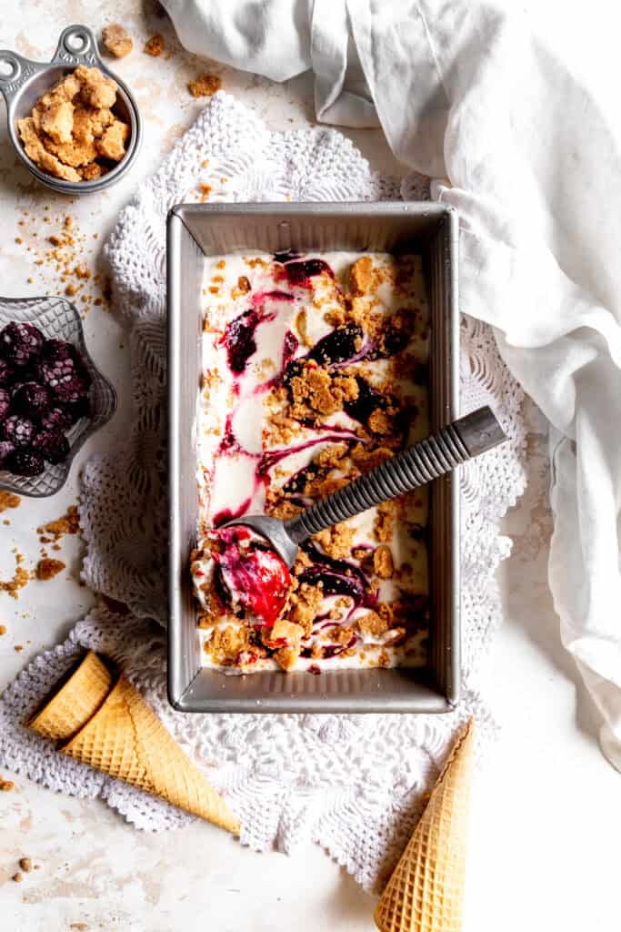 Ice cream scoop in a pan of blackberry cobbler ice cream.