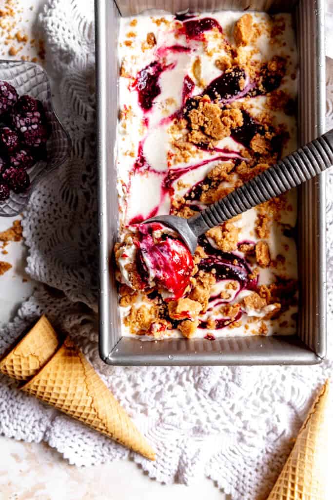 Ice cream scoop in a pan of blackberry cobbler ice cream and sugar cones.