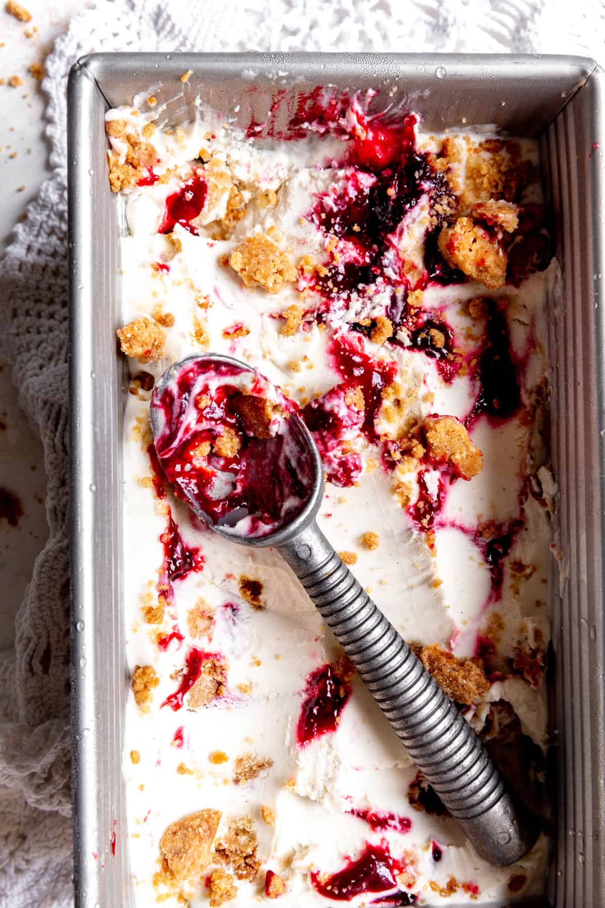 Ice cream scoop covered in blackberry compote sitting in a pan of ice cream.