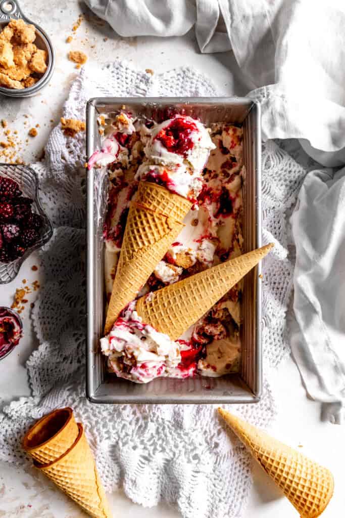 Sugar cones topped with scoops of blackberry cobbler ice cream lying in a pan.