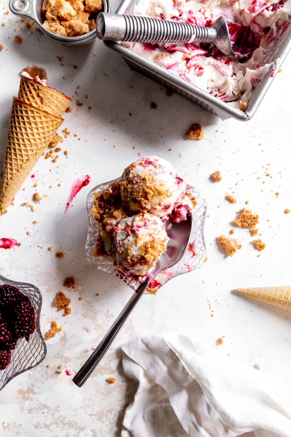 Bowl of blackberry cobbler ice cream, a linen napkin and scattered sugar cones.