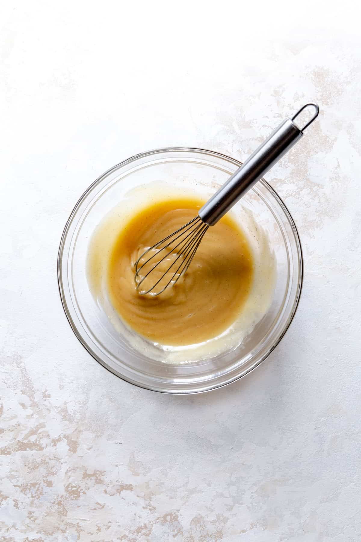 Glass bowl of vegan sweetened condensed milk and a wire whisk.
