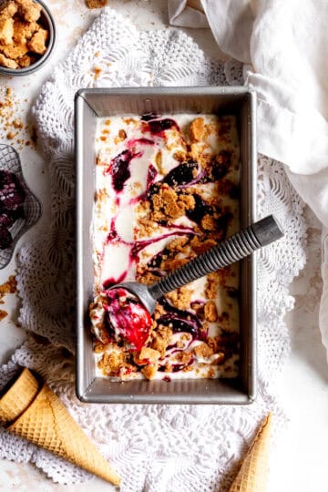 Ice cream scoop in a pan of blackberry cobbler ice cream and a cup of blackberries.
