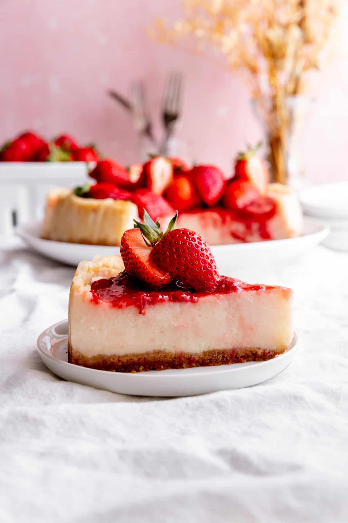 Slice of cheesecake topped with strawberries on a white plate.