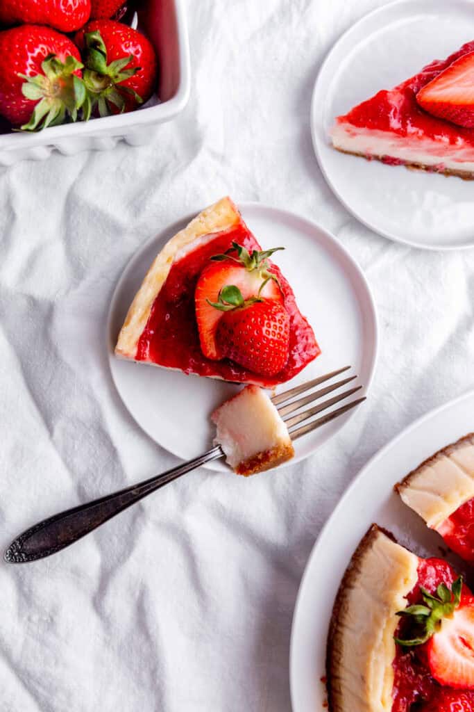 Fork cutting into a slice of cheesecake on a white plate.