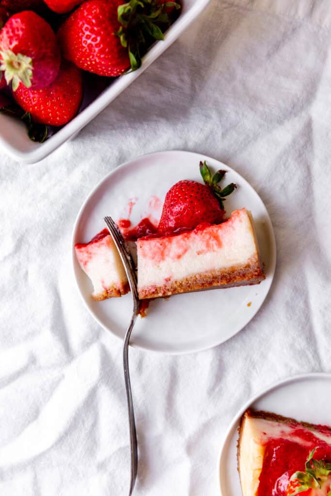 Fork cutting into a slice of cheesecake and a basket of strawberries.