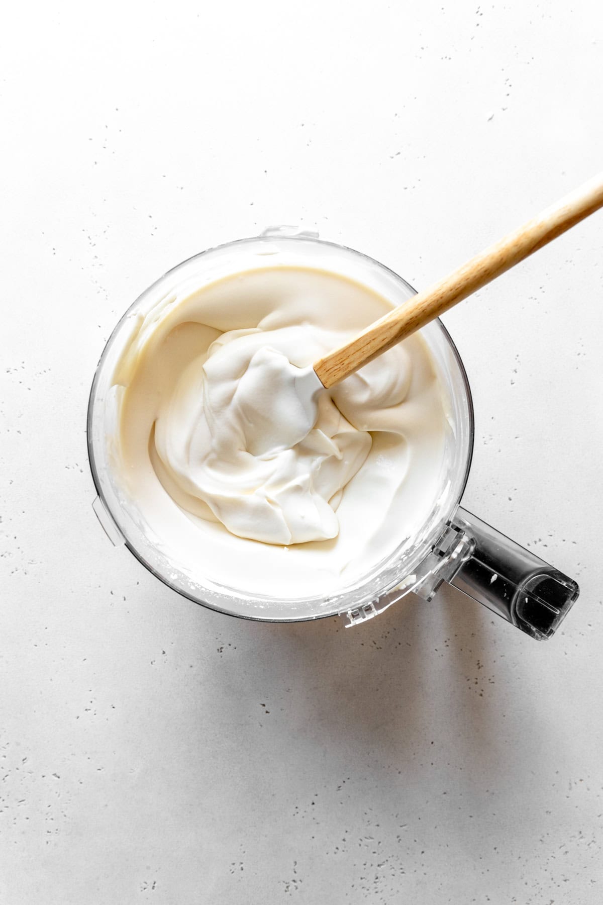 Cheesecake filling in a food processor with a rubber spatula.
