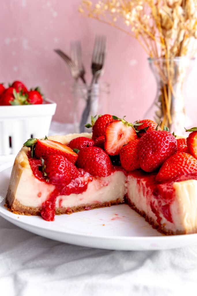 Cheesecake topped with strawberries and a vase of flowers.