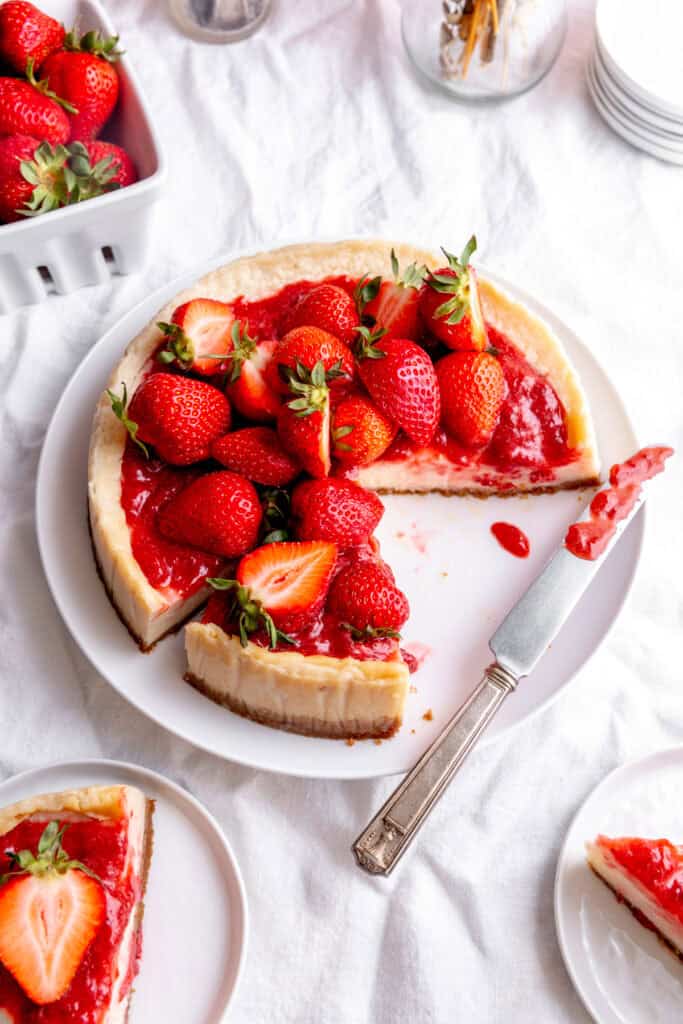 Cheesecake with slices missing and a knife covered in strawberry sauce.