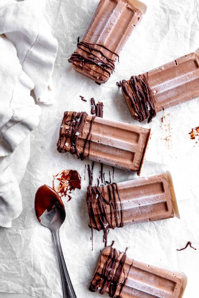 Fudge pops lying on parchment paper and a spoon covered in chocolate.