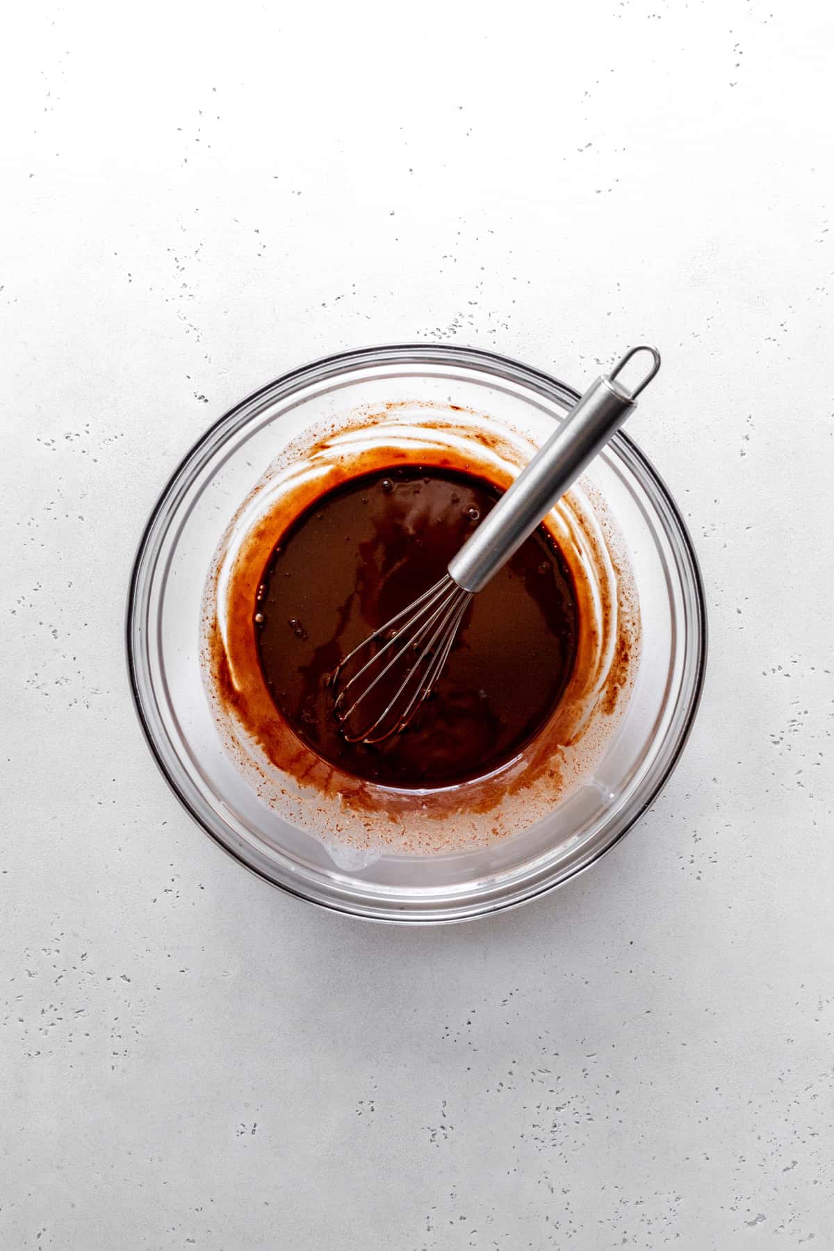 Melted chocolate in a glass bowl with a whisk.