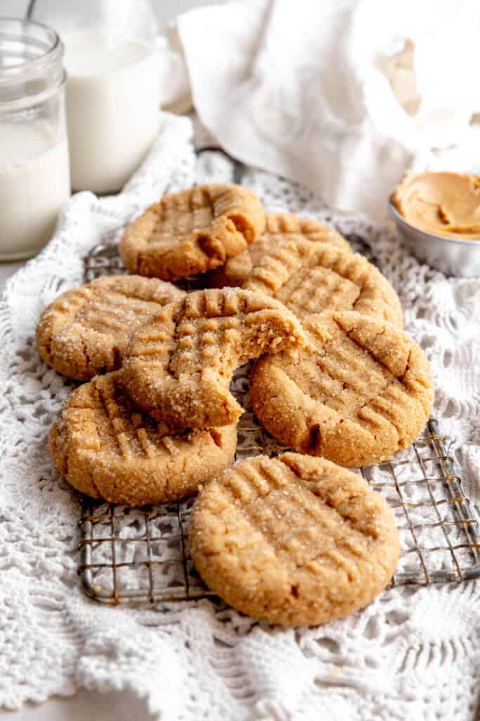 Pile of peanut butter cookies, a jug of milk and a cup of creamy peanut butter.