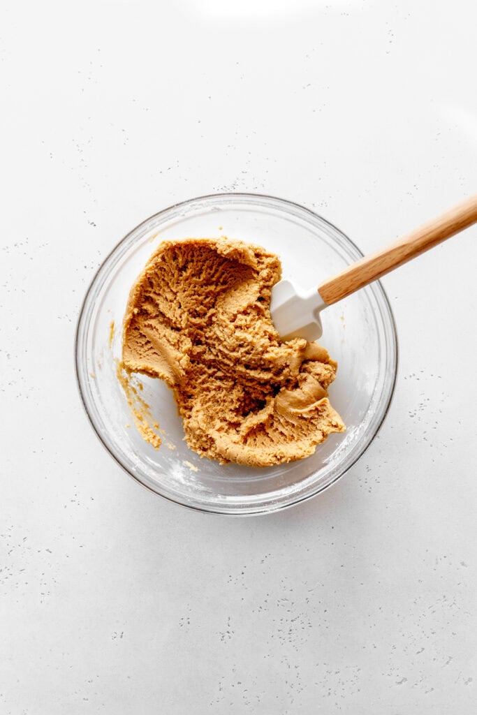 Peanut butter cookie dough in a glass bowl with a rubber spatula.