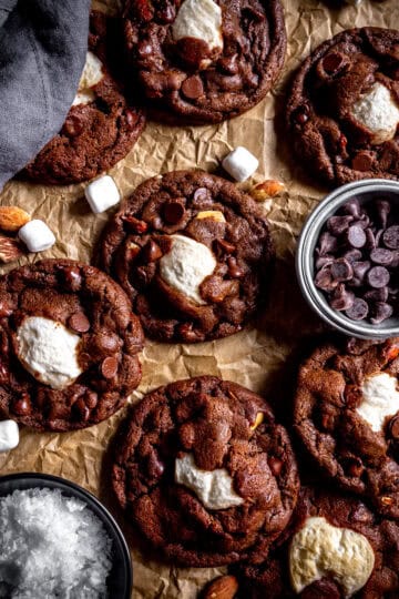 Rocky road cookies on a baking sheet, a cup of chocolate chips and a cup of sea salt.