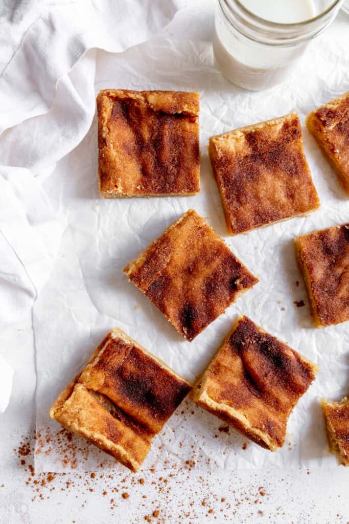 Snickerdoodle bars arranged on white parchment with a glass of milk.