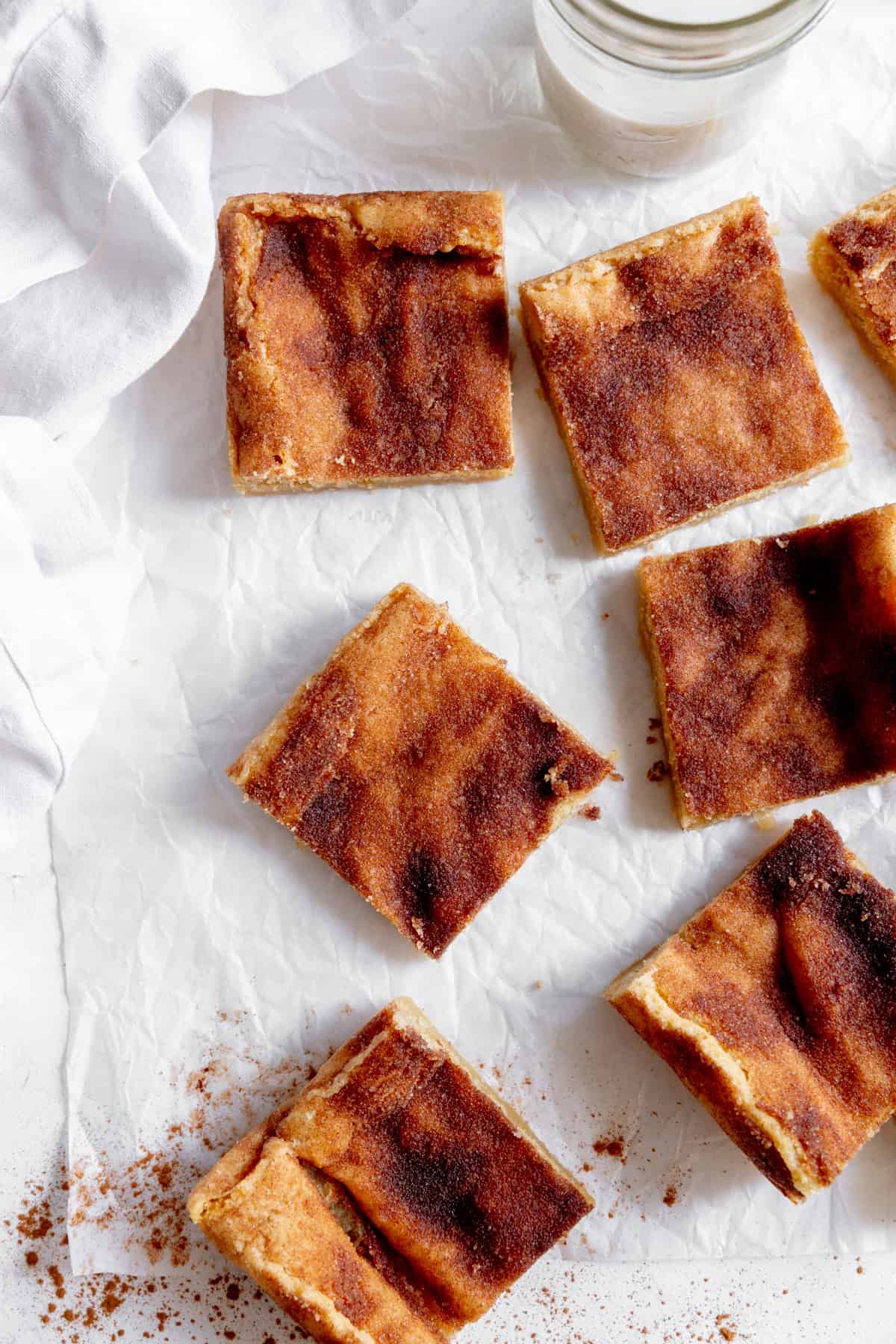 Snickerdoodle bars arranged on white parchment with a glass of milk.