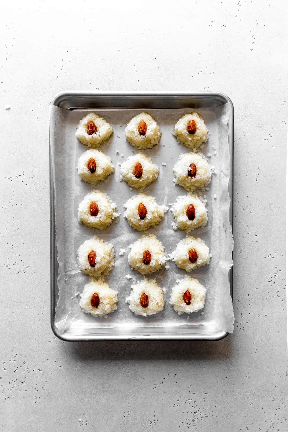 Scoops of coconut filling on a baking sheet with almonds pressed into the center of each.