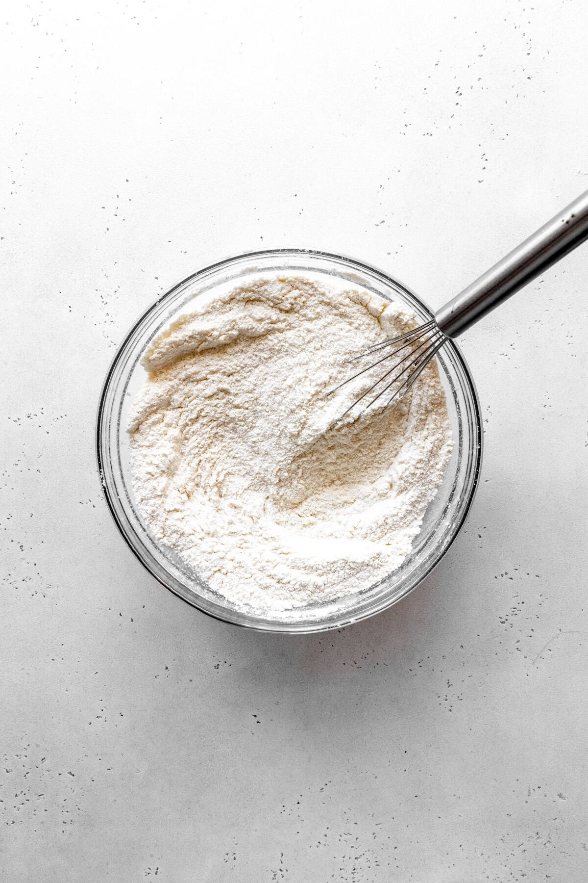 Dry cake ingredients in a glass bowl with a wire whisk.
