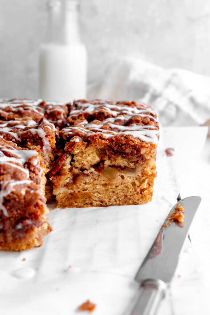 Apple cinnamon coffee cake, a knife, a linen napkin and a jug of milk.
