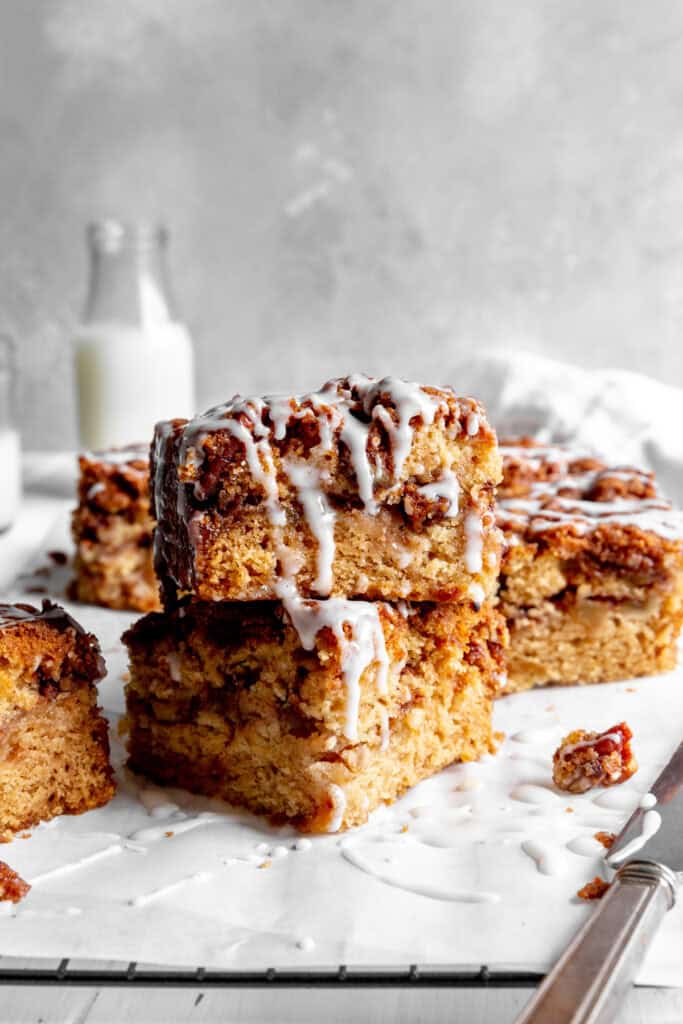Stacked slices of apple cinnamon coffee cake drizzled in glaze and a jug of milk.