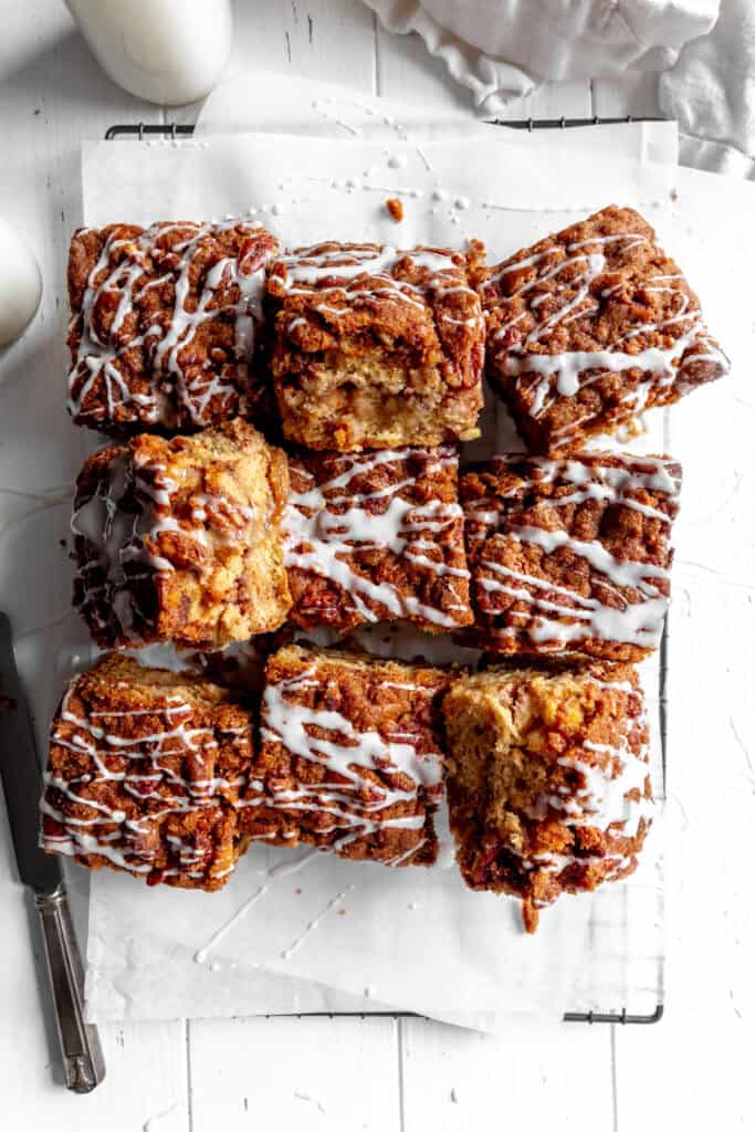 Sliced apple cinnamon coffee cake on a wire rack, a linen napkin and a jug of milk.