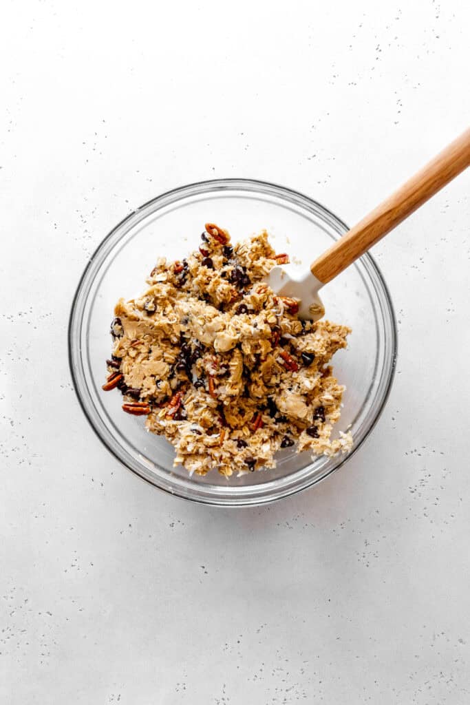 Cowboy cookie dough in a glass bowl with a rubber spatula.
