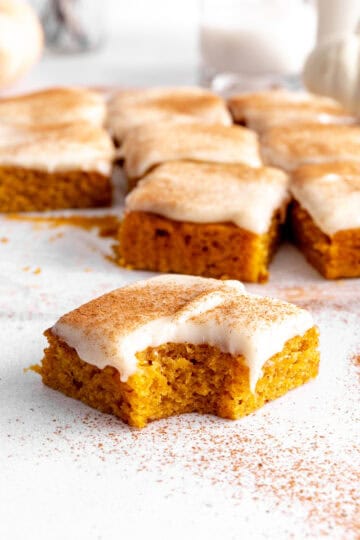 Pumpkin bar with cream cheese frosting with a bite taken out of it.