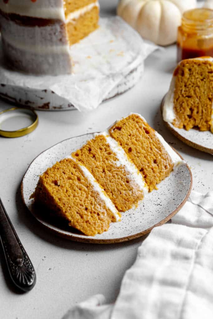 Slice of pumpkin layer cake on a plate and a white pumpkin.