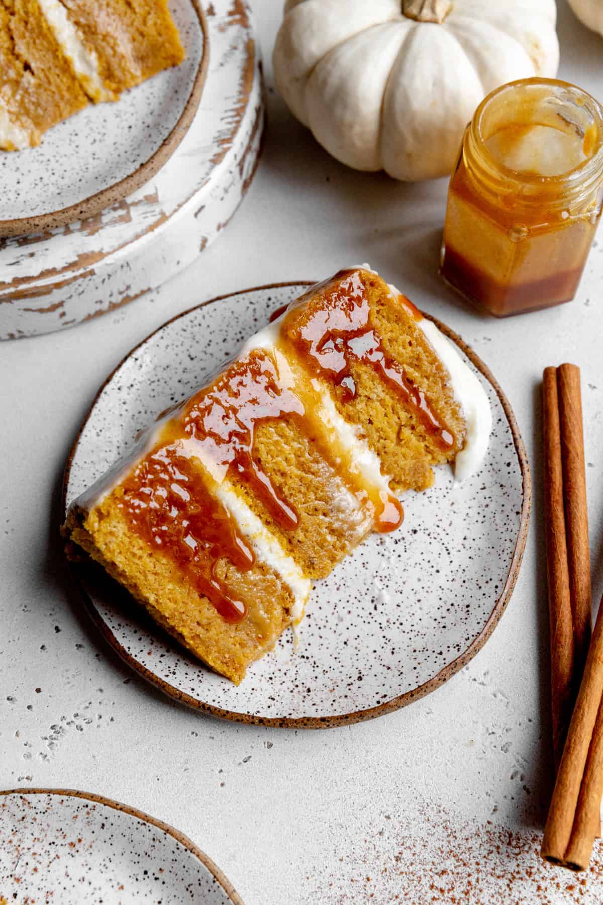 Slice of pumpkin layer cake drizzled in caramel sauce surrounded by cinnamon sticks.