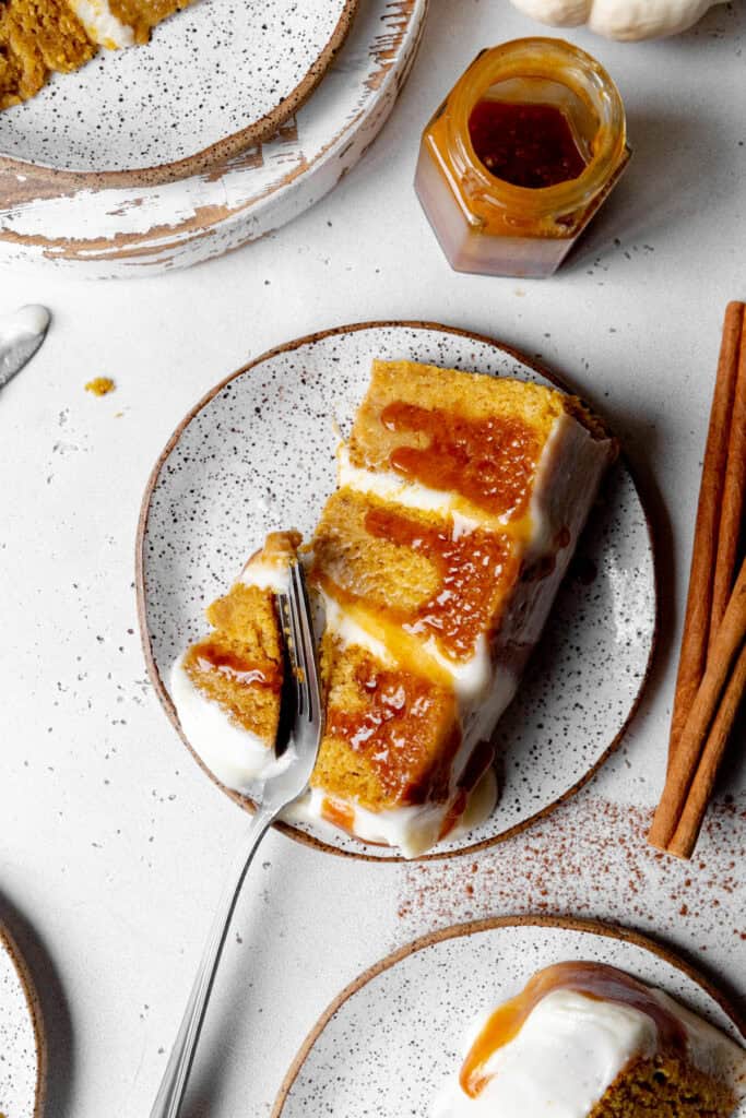 Fork cutting into a slice of pumpkin layer cake drizzled in caramel sauce.
