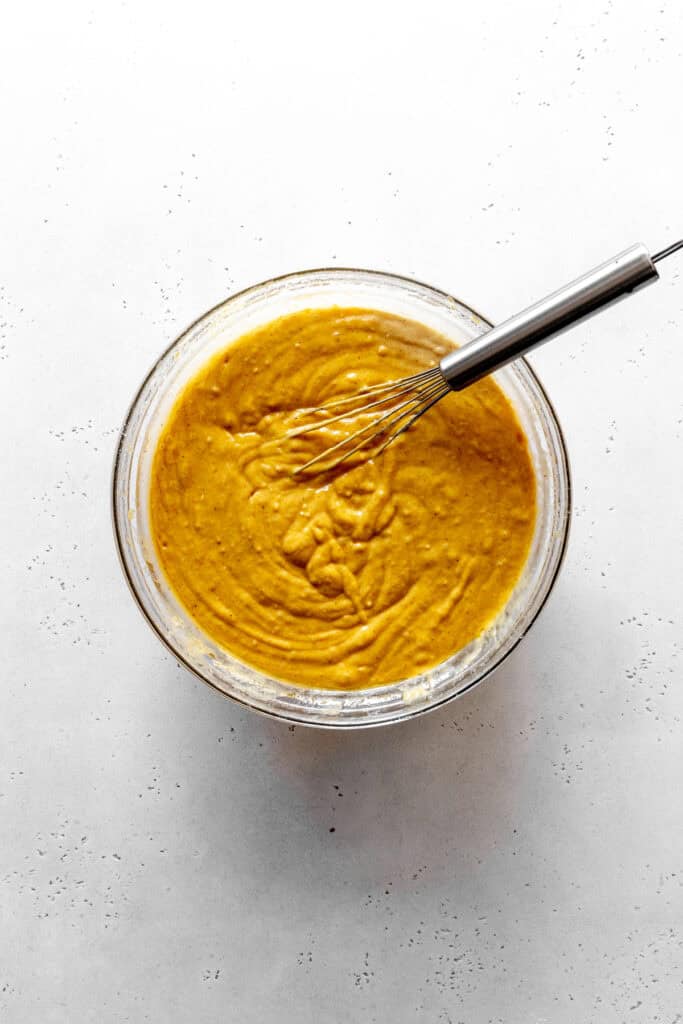 Bowl of pumpkin cake batter in a glass bowl with a wire whisk.