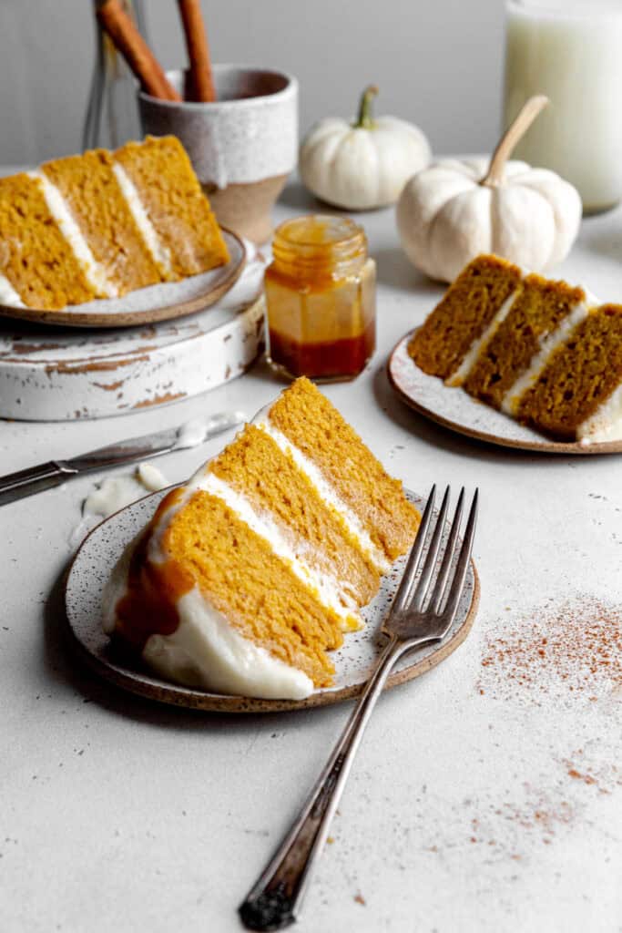 Slices of pumpkin cake on white plates, a jug of milk and a cup of cinnamon sticks.