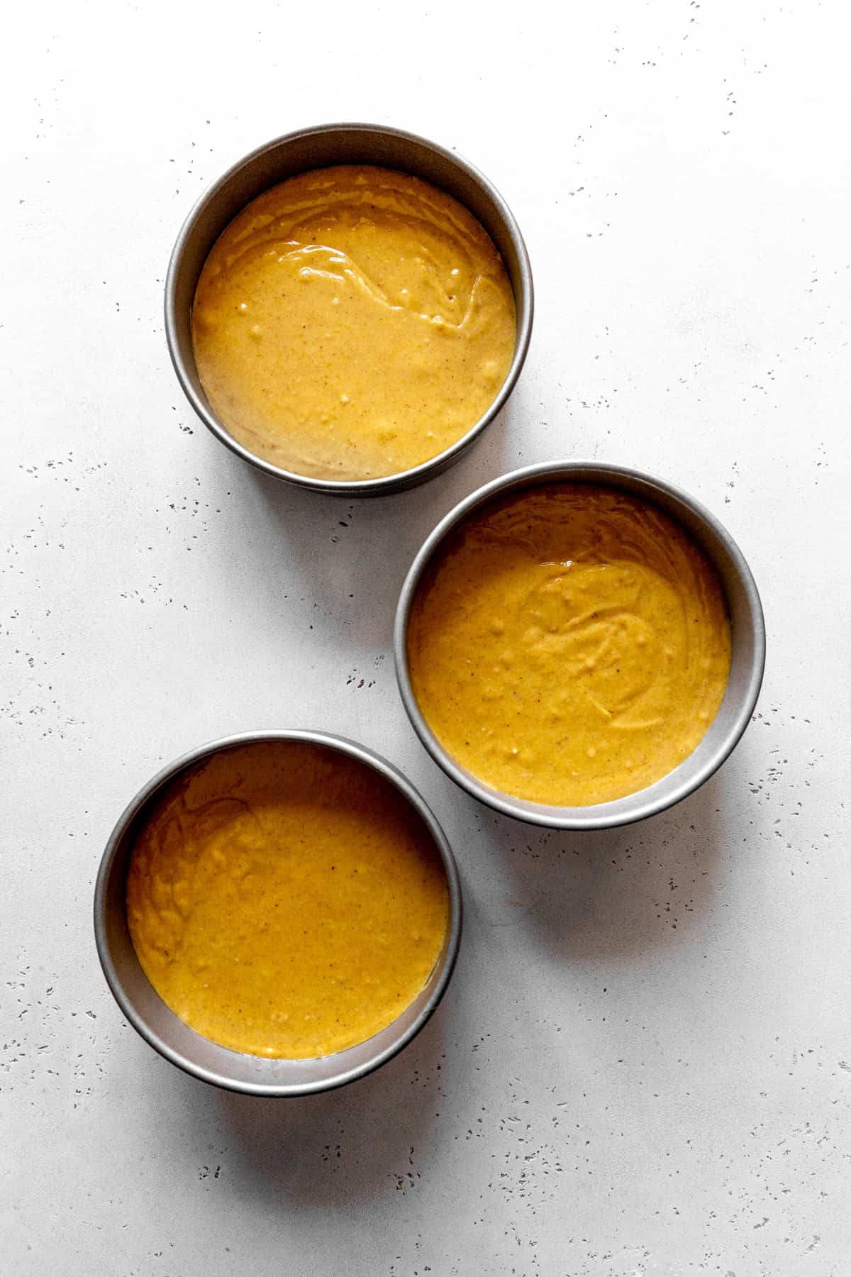 Three round cake pans filled with pumpkin cake batter.