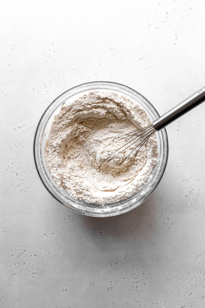 Flour in a glass bowl with a wire whisk.