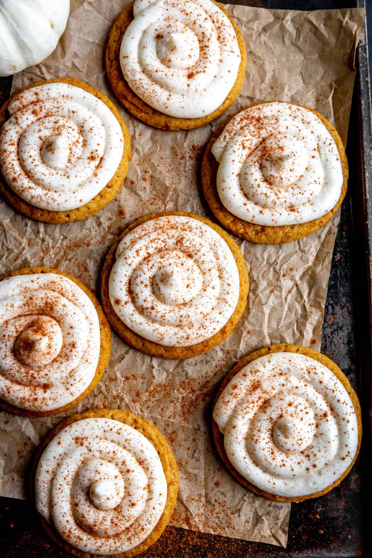 Frosted pumpkin cookies on a baking sheet with a small white pumpkin.