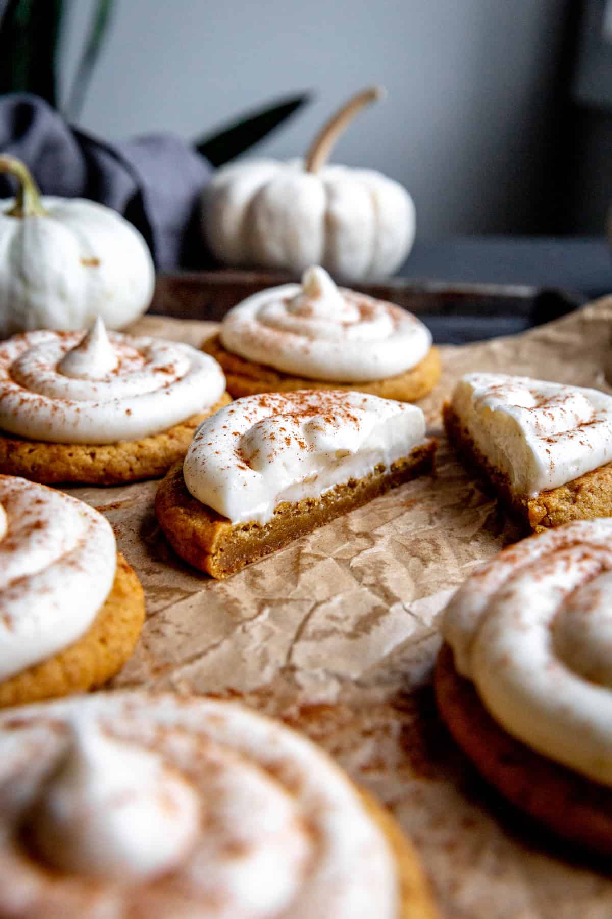 Frosted pumpkin cookie cut in half and two small white pumpkins.