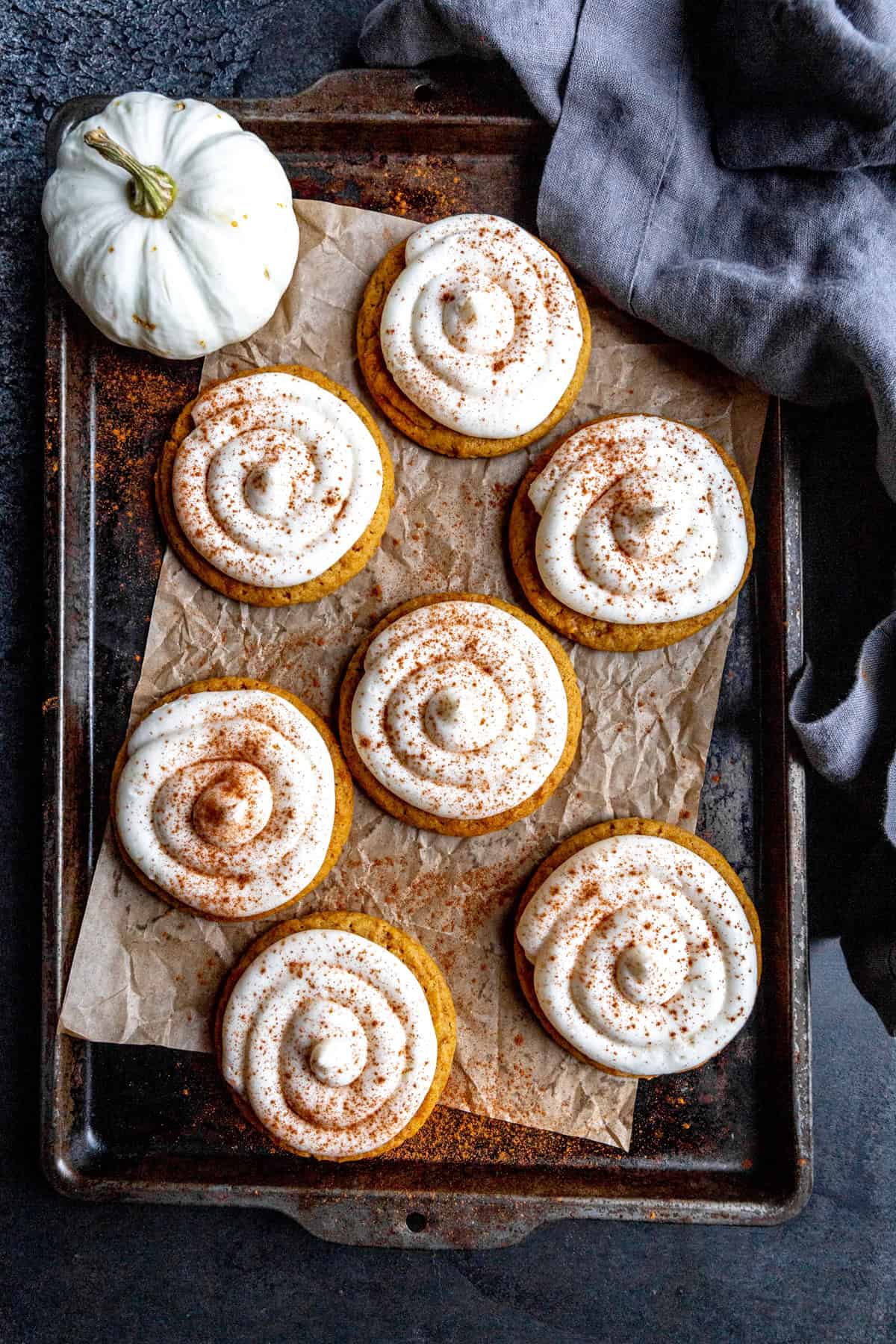 Frosted pumpkin cookies on a baking sheet with a small white pumpkin.