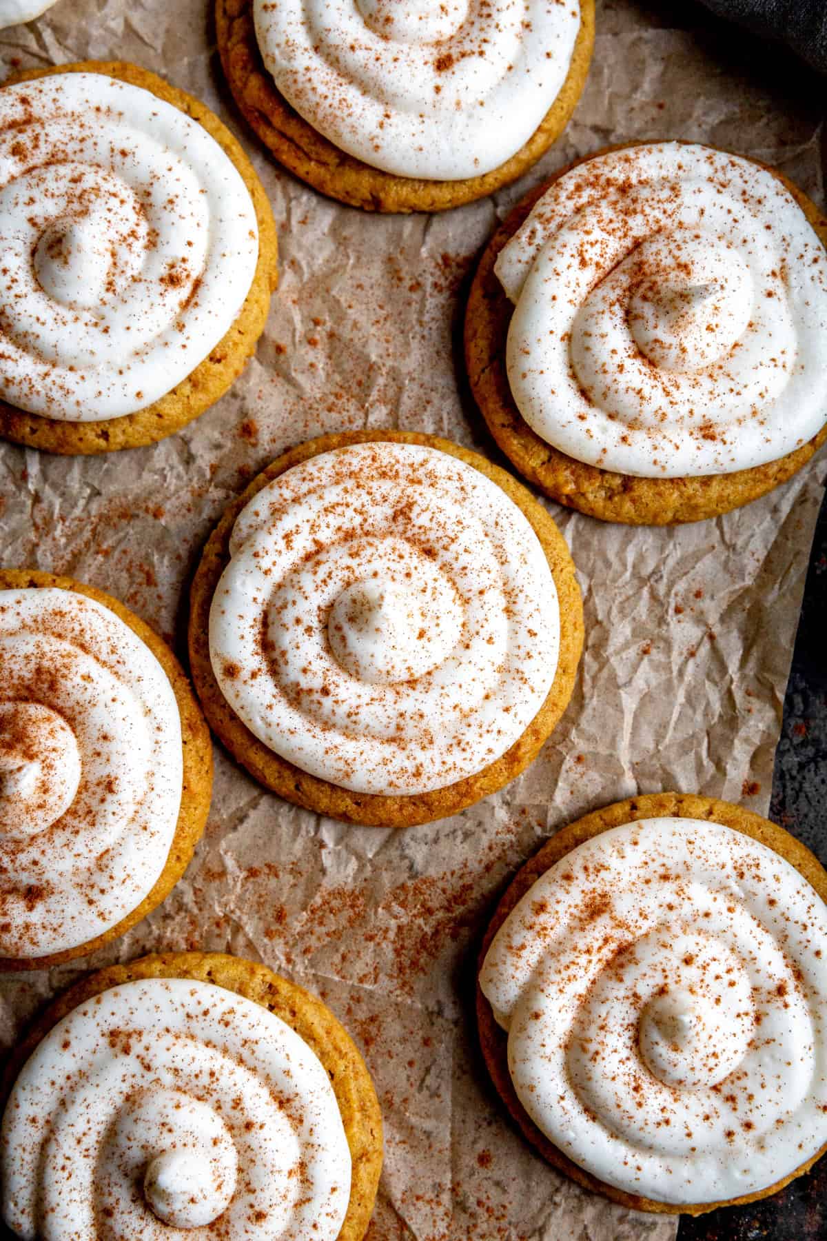 Frosted pumpkin cookies on brown parchment paper.