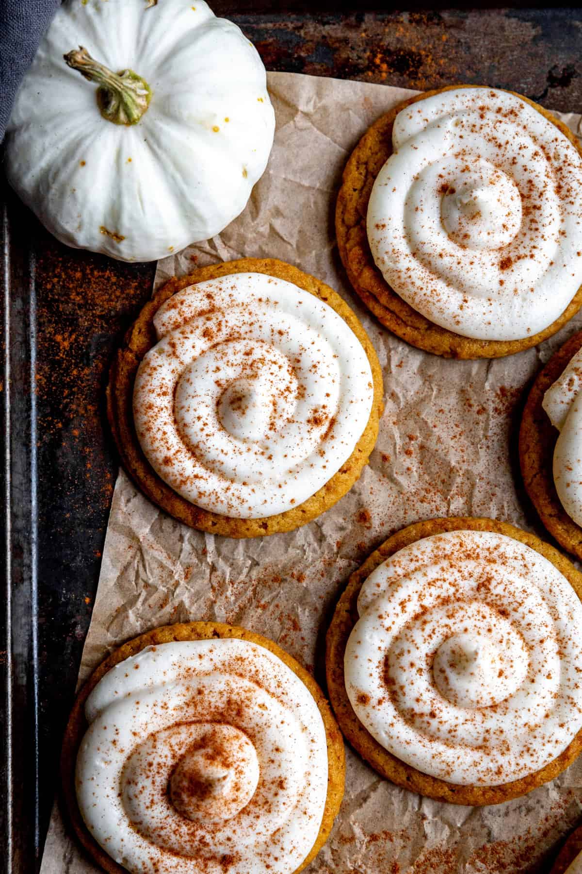 Frosted pumpkin cookies on a baking sheet with a small white pumpkin.