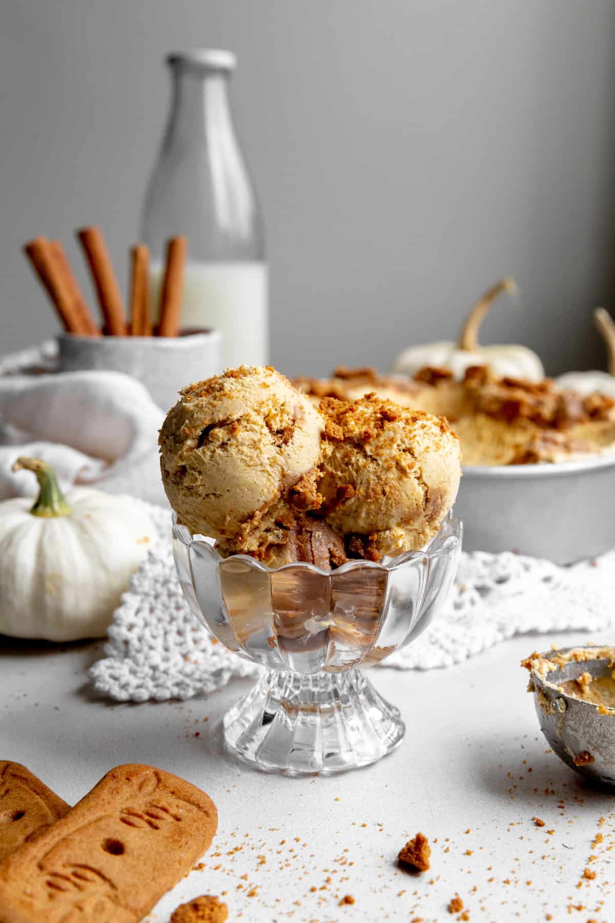 Dish of pumpkin spice ice cream, a jug of milk and a cup of cinnamon sticks.