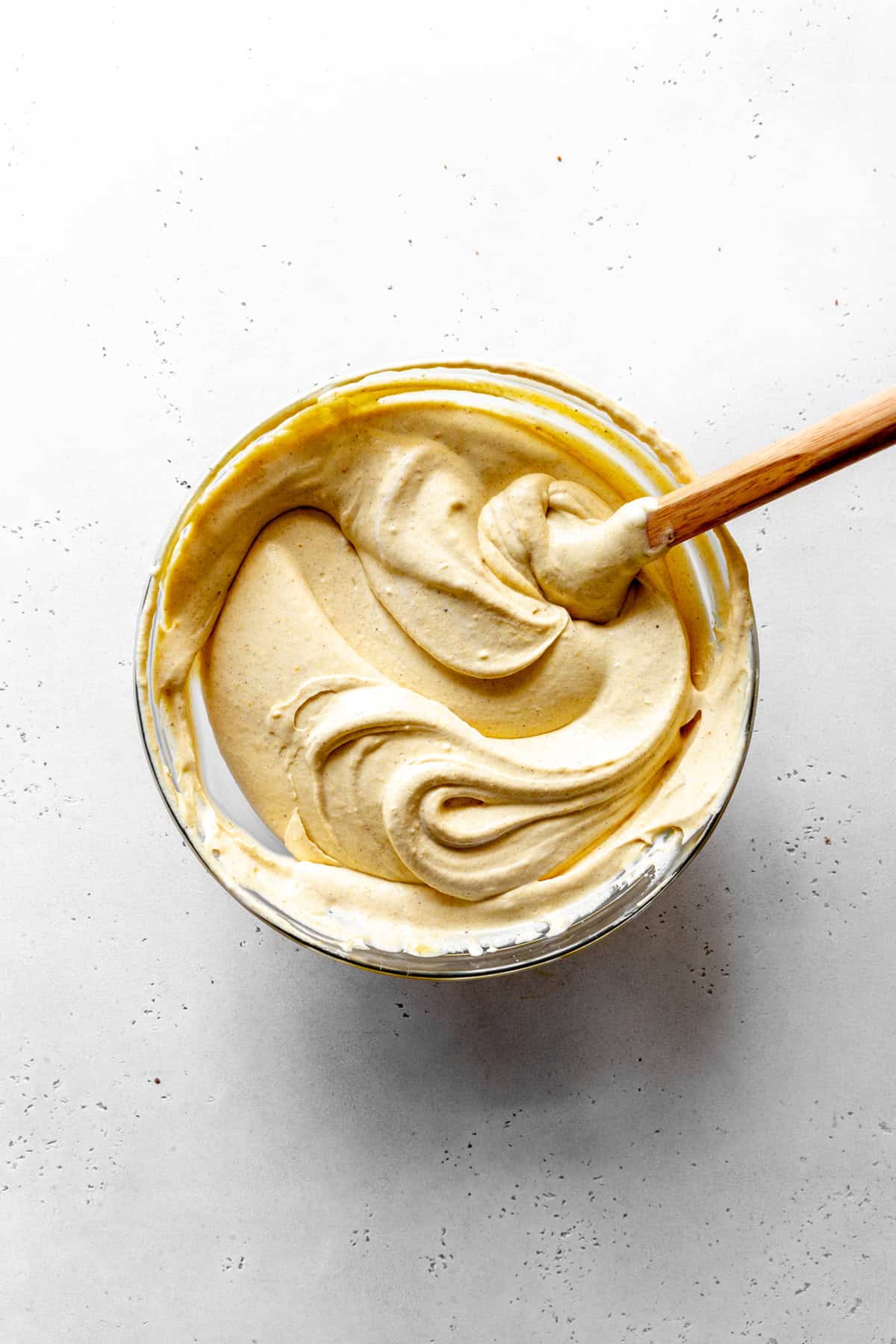 Pumpkin spice ice cream base in a glass bowl with a rubber spatula.