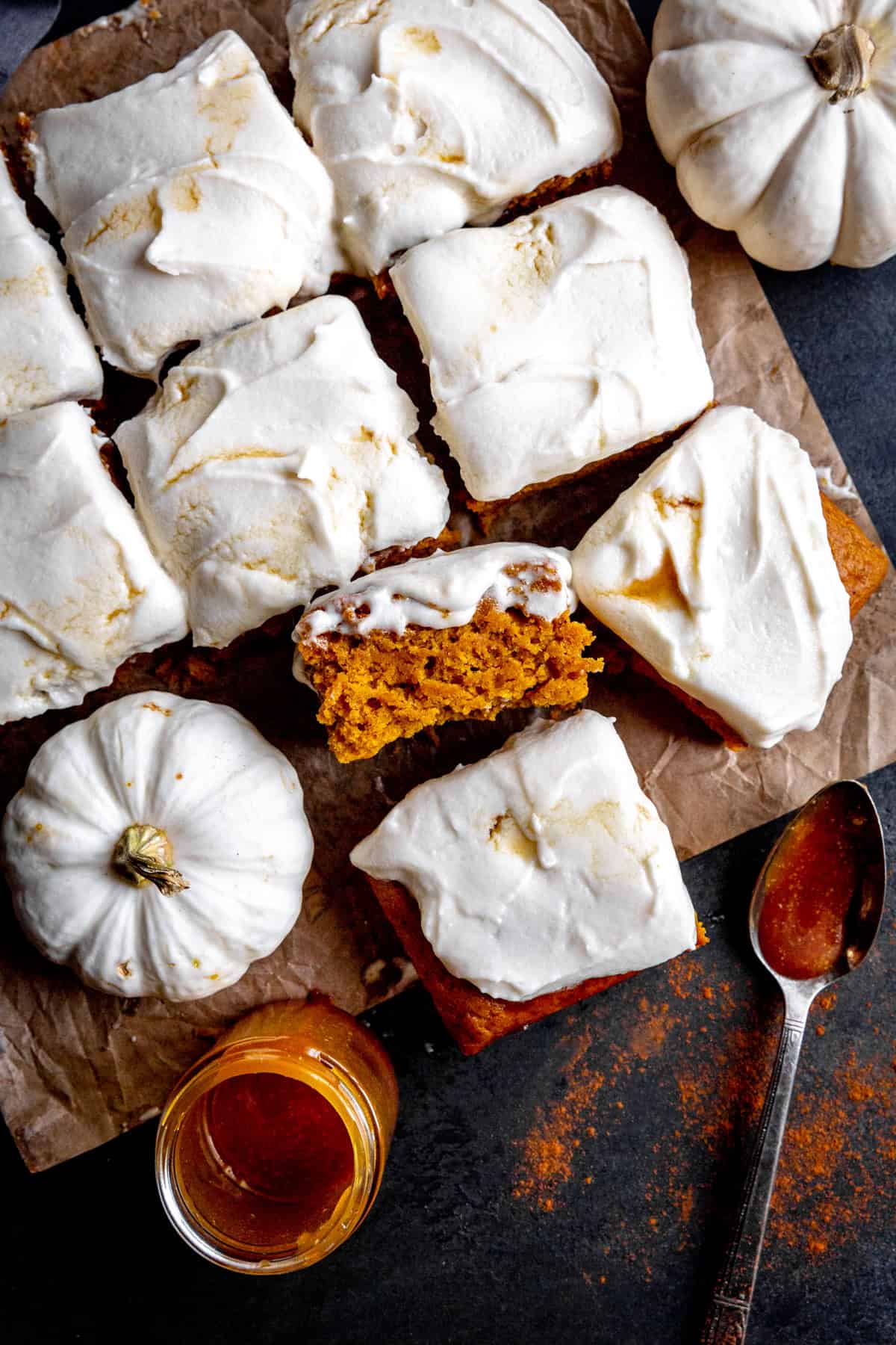 Frosted pumpkin cake squares, small white pumpkins and a jar of caramel sauce.