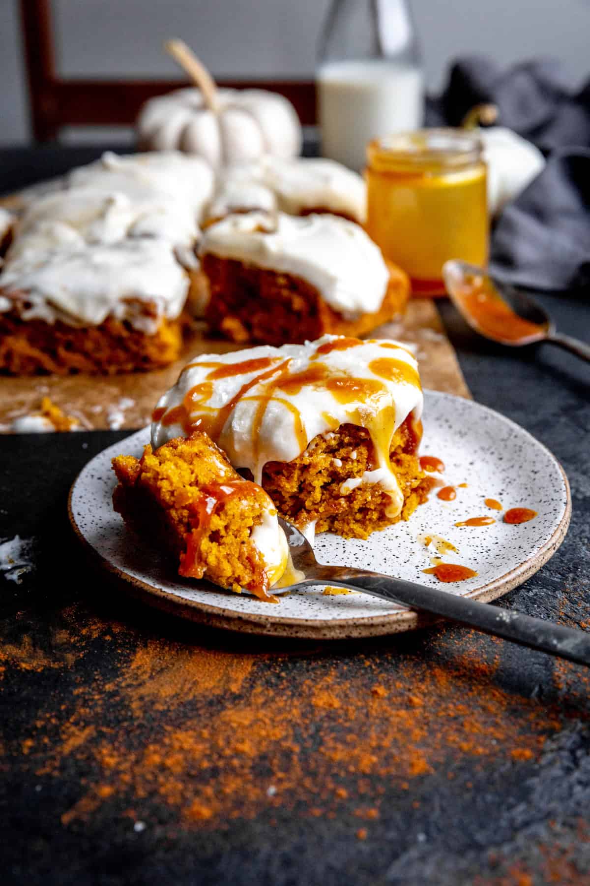 Slice of pumpkin cake drizzled with caramel on a white plate with a fork.