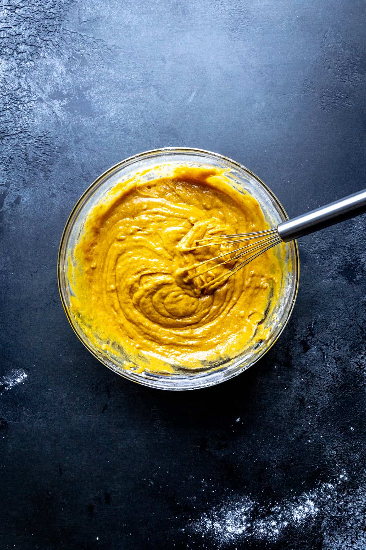 Glass bowl of pumpkin cake batter and a wire whisk.
